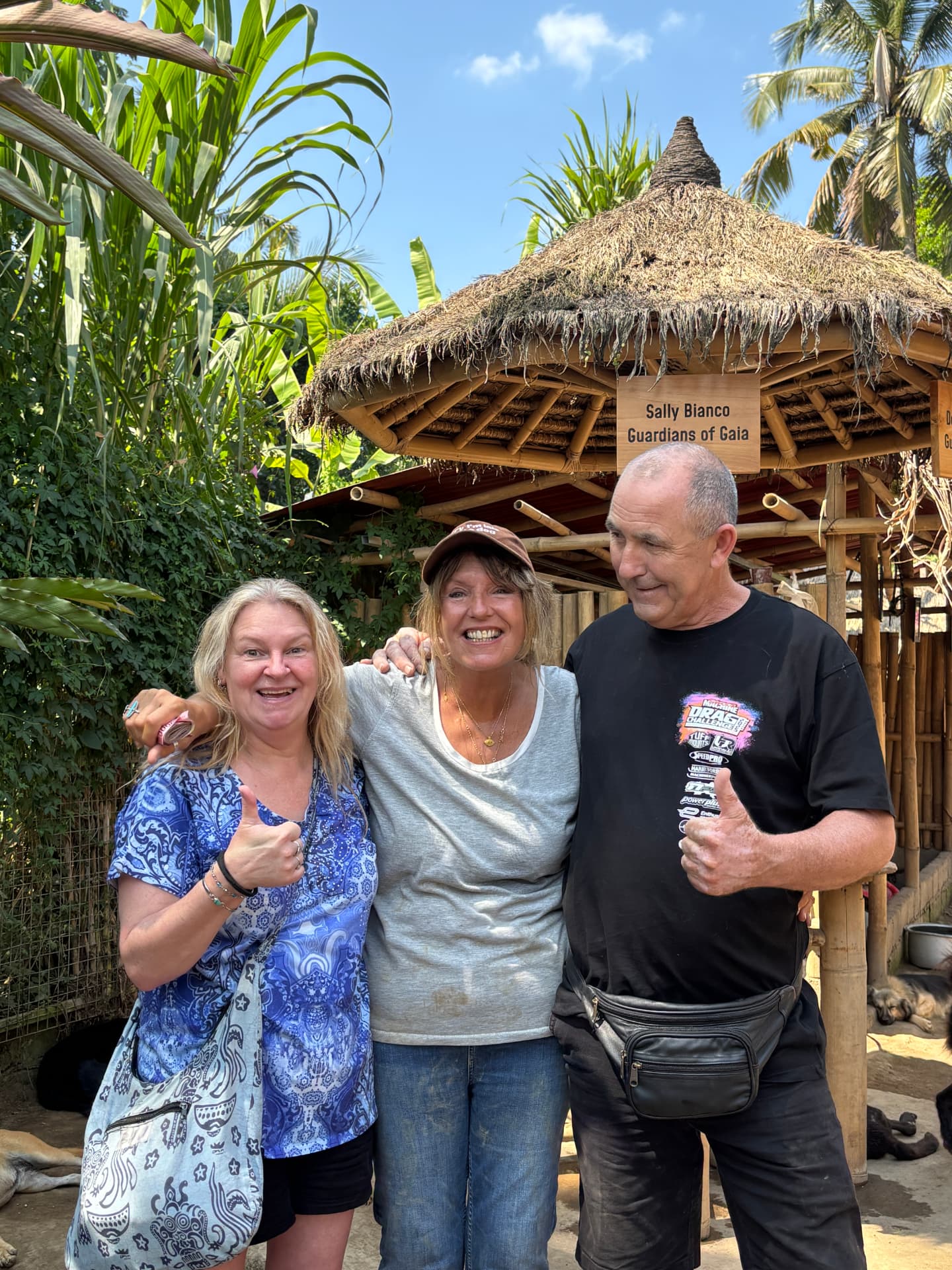 Three smiling visitors posing under a thatched-roof shelter at the GAIA sanctuary