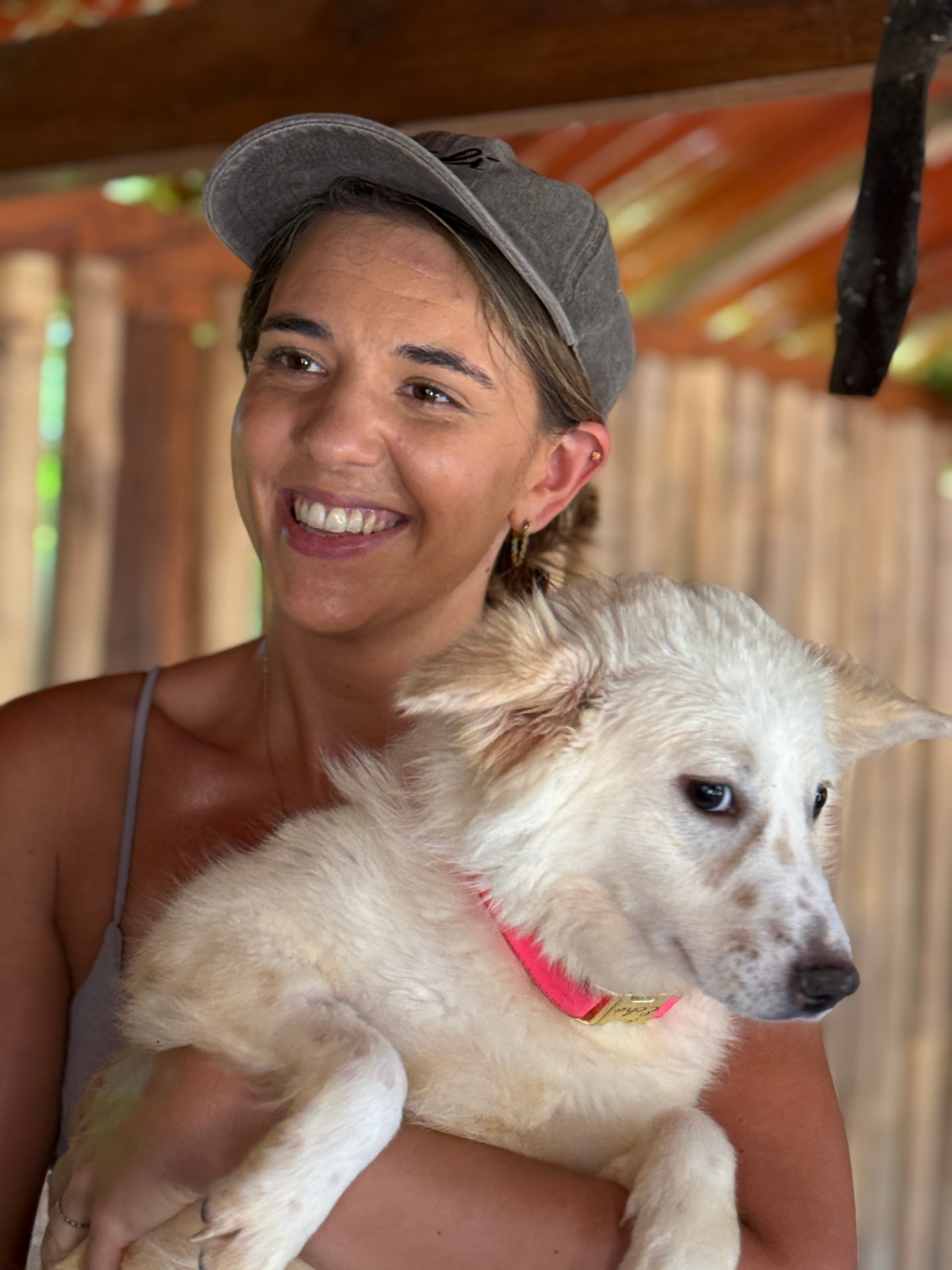 A visitor in a grey cap holding a white dog with brown spots in front of a bamboo wall