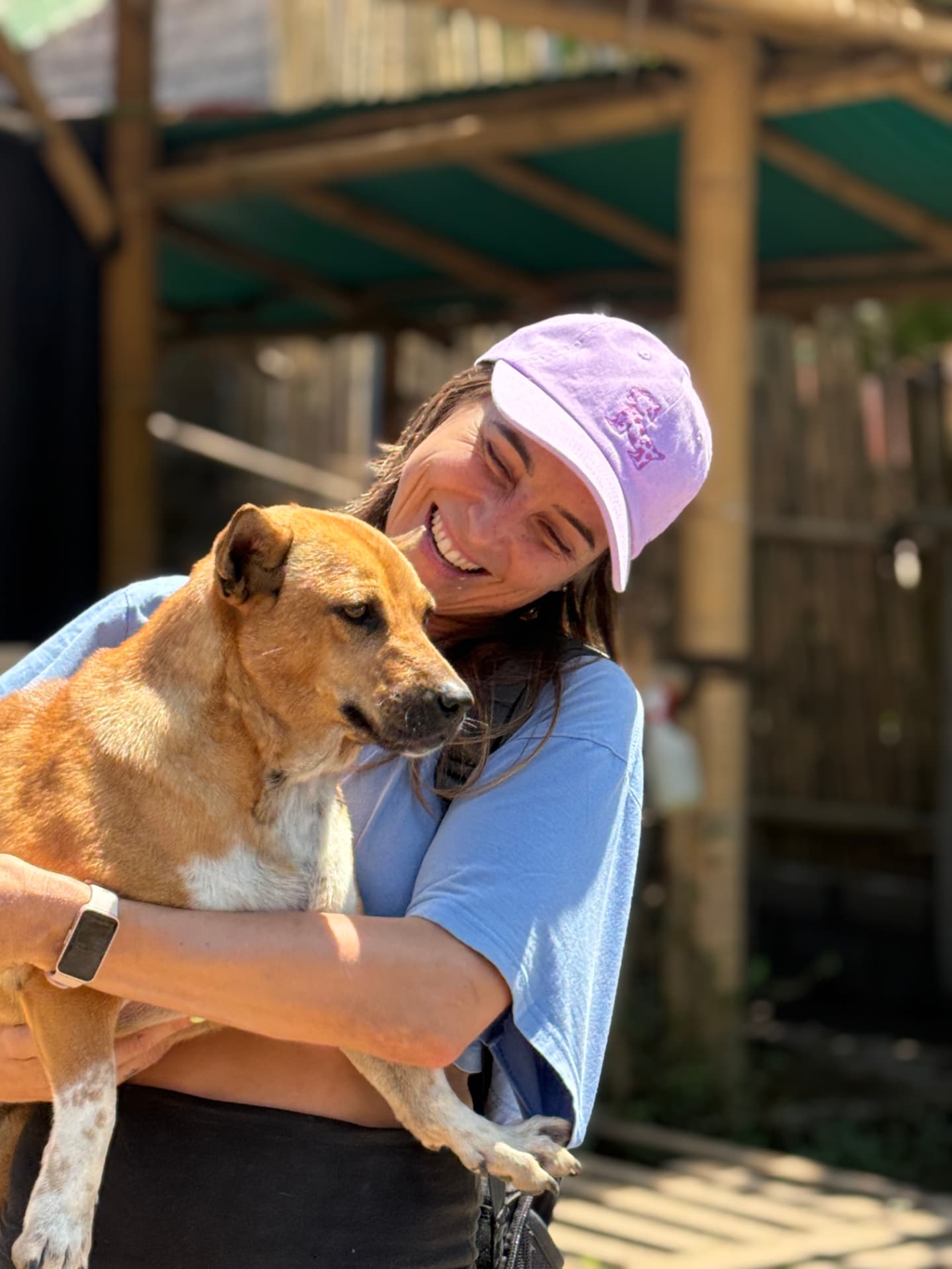 A visitor in a purple cap hugging a tan and white dog
